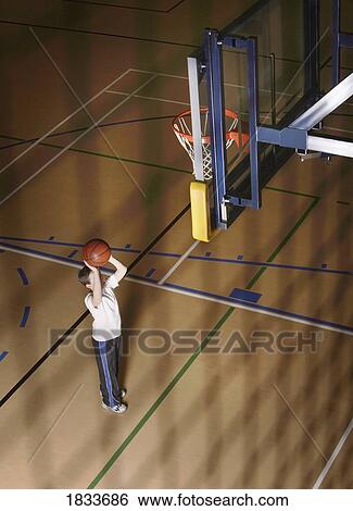 Stock Photograph - Boy aiming ball at basketball net. Fotosearch