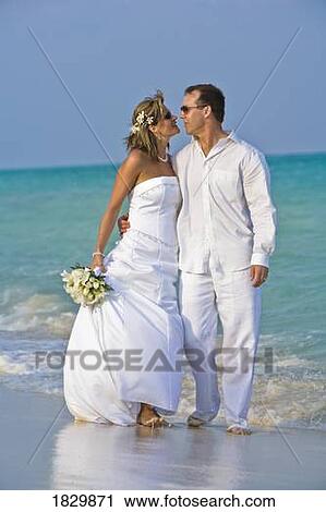 Stock Image - Bride and groom embracing on beach. Fotosearch