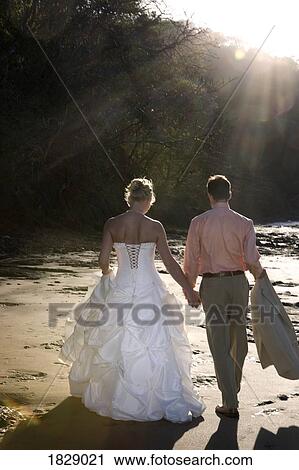 Stock Image - Bride and groom holding hands on beach. Fotosearch