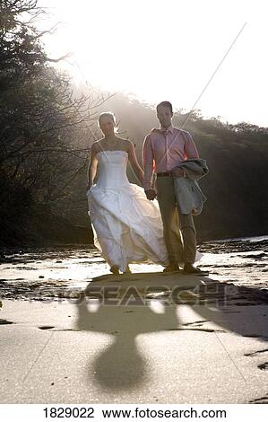 Stock Image - Bride and groom holding hands on beach. Fotosearch