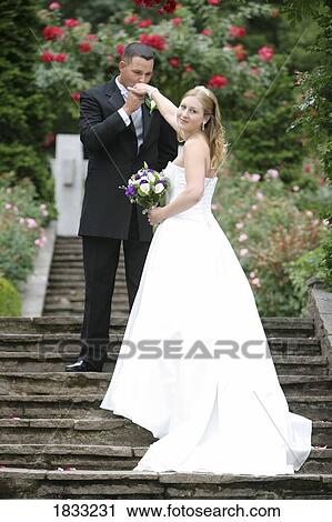 Stock Image - Bride and groom on stone stairs in rose garden. Fotosearch