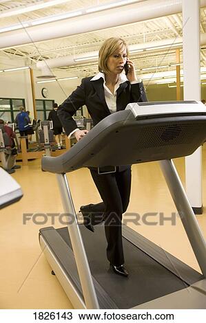 Stock Image - Businesswoman using cell phone on treadmill. Fotosearch