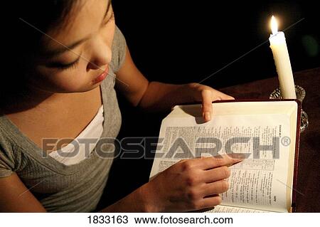 Stock Image - Girl reading the Bible by candlelight. Fotosearch