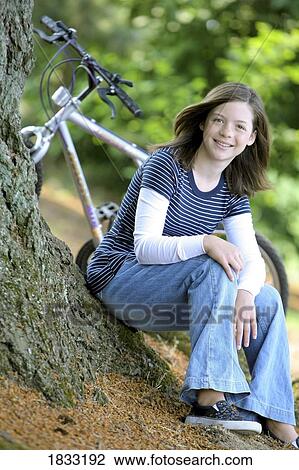 Stock Image - Girl sitting by tree with bike. Fotosearch