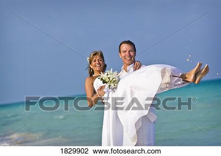 Groom carrying bride on beach View Large Photo Image Stock Image - Groom carrying bride on beach. Fotosearch