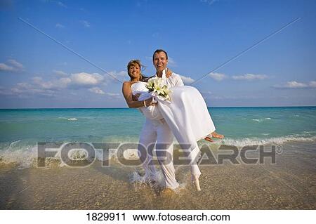 Groom carrying bride on beach View Large Photo Image Stock Image - Groom carrying bride on beach. Fotosearch