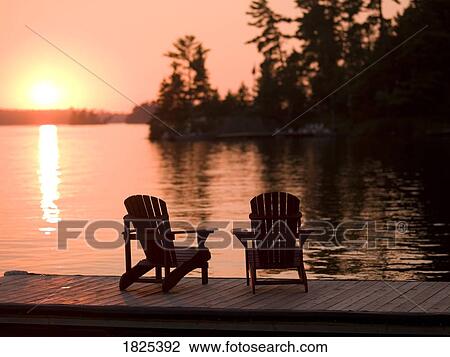 Stock Image - Lake of the Woods, Ontario, Canada, Adirondack chairs on a dock facing the sunset. Fotosearch