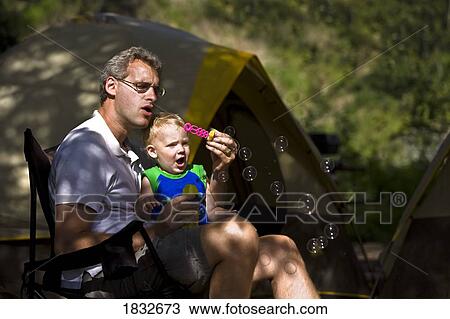 Stock Image - Man and son blowing bubbles . Fotosearch