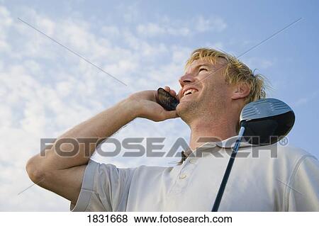 Stock Photo - Man holding golf club, speaking on cell phone . Fotosearch