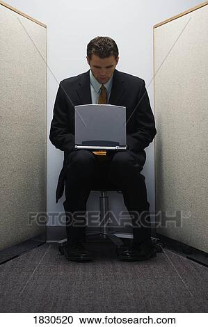 Stock Image - Man on laptop in tiny cubicle. Fotosearch