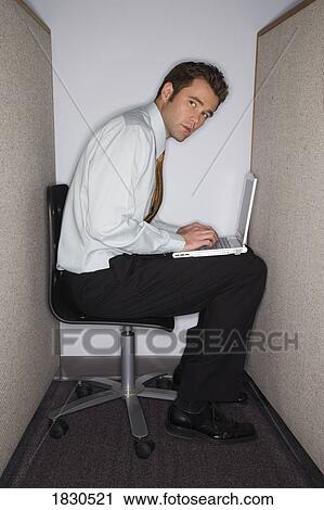 Stock Image - Man on laptop in tiny cubicle. Fotosearch