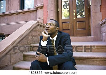 Stock Photography - Man sitting in front of brownstone, Harlem, New York City, New York, USA. Fotosearch