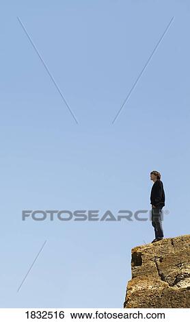 Stock Photograph - Man Standing On The Edge Of A Cliff With His Arms Outstretched. Fotosearch