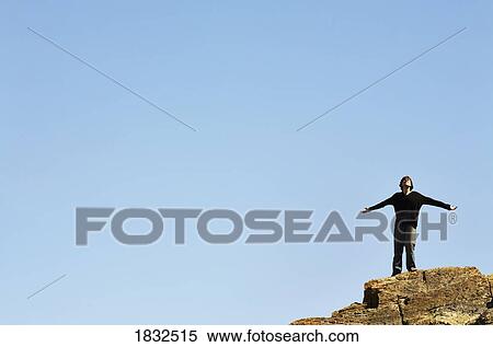 Stock Photography - Man Standing On The Edge Of A Cliff With His Arms Outstretched. Fotosearch