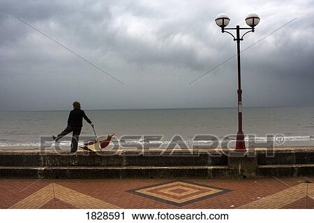 Stock Image - Man with umbrella standing by boardwalk, Yorkshire, England. Fotosearch