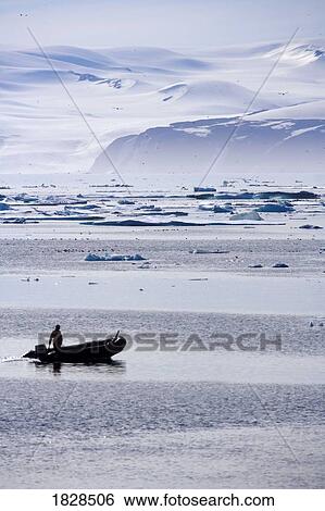 Stock Photograph - Person in boat by ice berg off coast of Nunavut, Canada. Fotosearch