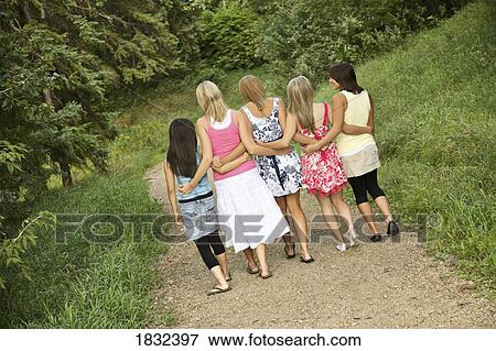 Stock Photo - Rear view of girl friends walking on a path. Fotosearch