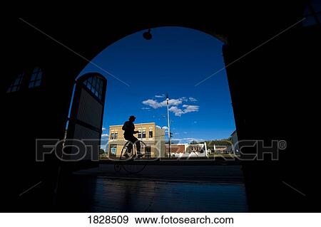 Stock Photo - Silhouette of man riding old fashioned bicycle down small town street. Fotosearch