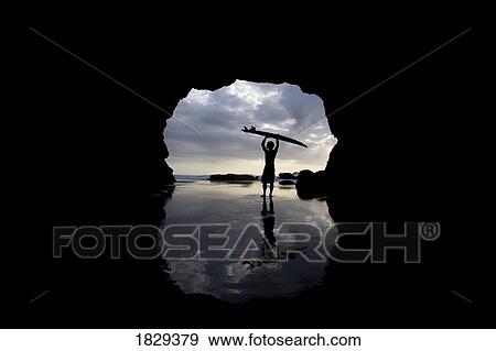 Stock Photo - Surfer emerging from cave, Muriwai, North Island, West Auckland, New Zealand. Fotosearch