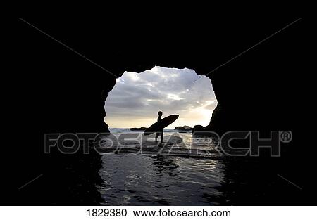 Stock Image - Surfer inside a cave at Muriwai, New Zealand. Fotosearch