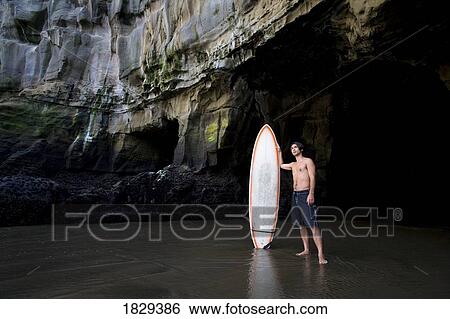 Stock Photograph - Surfer inside a cave at Muriwai, New Zealand. Fotosearch