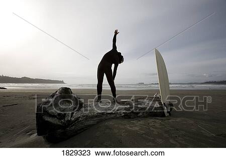 Stock Image - Surfer stretching on beach. Fotosearch