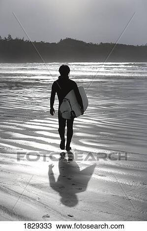 Stock Image - Surfer walking on beach, Cox Bay near Tofino, British Columbia, Canada. Fotosearch