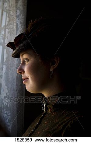 Stock Photo - Woman in vintage clothes looking through window. Fotosearch