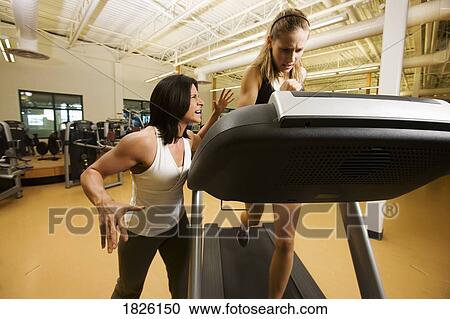 Stock Image - Woman running on treadmill with strong encouragement from trainer. Fotosearch