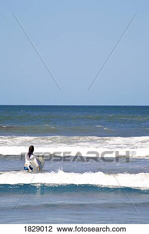 Stock Image - Woman taking surfboard into sea. Fotosearch