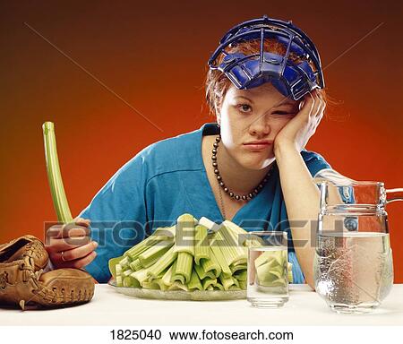 Stock Image - Woman wearing sports equipment and eating celery. Fotosearch