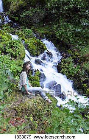 Young girl sitting by a waterfall View Large Photo Image Stock Photo - Young girl sitting by a waterfall. Fotosearch