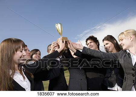 Group in business attire holding trophy View Large Photo Image Stock Photo - Group in business attire holding trophy. Fotosearch