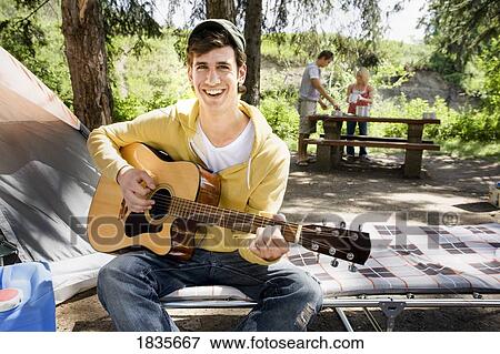 Stock Photo - Man playing an acoustic guitar at a campsite. Fotosearch