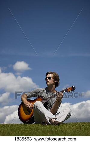 Stock Image - Man playing guitar on the grass. Fotosearch