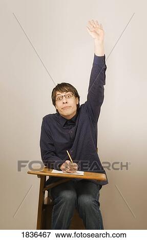 Stock Photo - Man raising hand sitting in school desk. Fotosearch