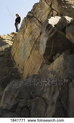 Man standing at top of cliff View Large Photo Image Stock Image - Man standing at top of cliff. Fotosearch