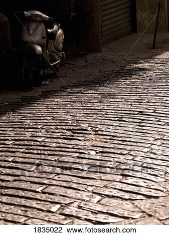 Stock Image - Moped in the shadows, cobblestone road, Naples, Italy. Fotosearch