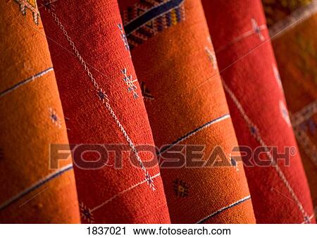 Stock Image - Red and orange Morrocan rugs hung for sale in the souks of Marrakech, Morocco . Fotosearch