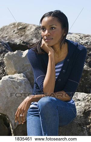 Stock Image - Woman sitting on rocks . Fotosearch