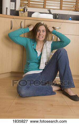 Stock Photo - Woman sitting on the floor of the kitchen. Fotosearch