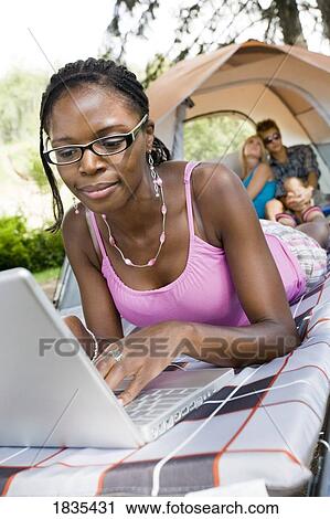 Stock Image - Woman working on computer while camping. Fotosearch
