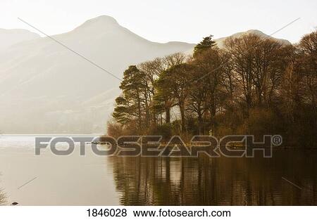 Stock Photo - Calm water with mountains and trees along the shoreline, England. Fotosearch