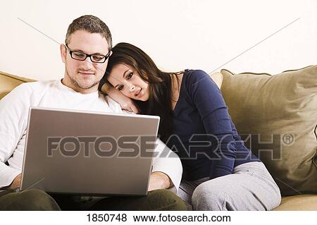 Stock Photo - Couple on sofa; Couple working on a laptop. Fotosearch