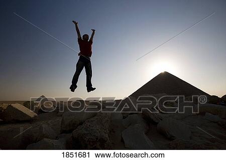 Stock Image - Dahshur, Egypt; Man jumping in the air in front of the Red Pyramid. Fotosearch