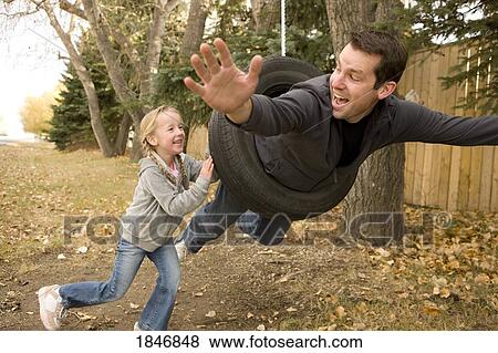 Stock Photo - Daughter pushing father on tire swing. Fotosearch