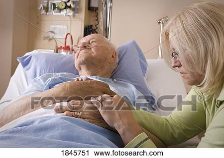 Stock Image - Elderly man and his daughter; Woman sitting by a man's hospital bed. Fotosearch