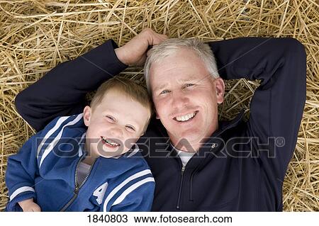 Stock Image - Father and son; Boy and his father lying in hay. Fotosearch