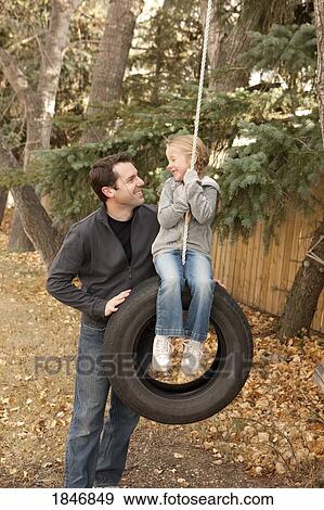 Stock Photo - Father pushing daughter on tire swing. Fotosearch