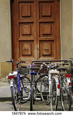 Picture - Florence, Italy; Bikes parked at a bike rack outside wooden doors. Fotosearch